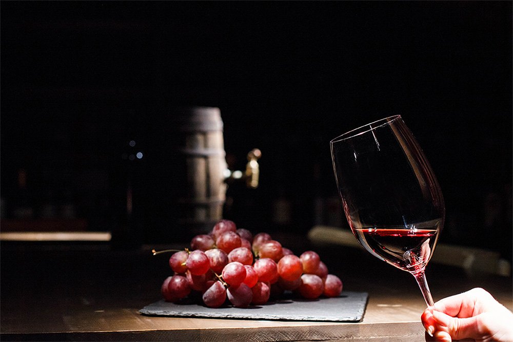 Taça de vinho próxima de um barril e uvas