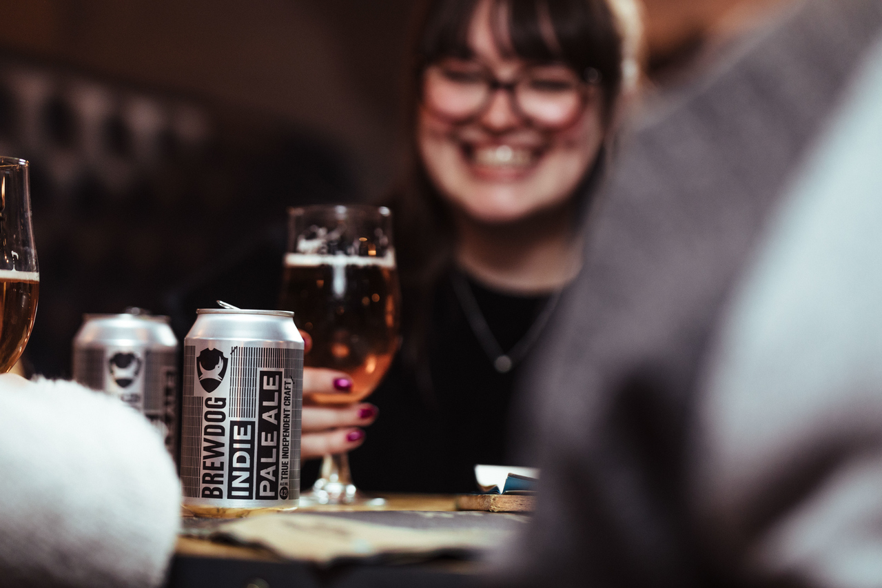 Duas latas de cerveja Brewdog, moça segurando um copo