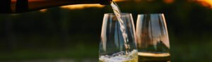 Taça com vinho branco envelhecido ao lado de garrafa de vinhos brancos antigos