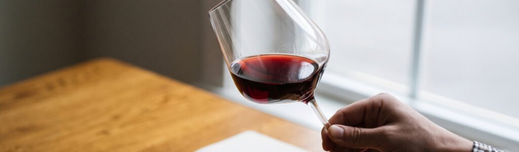Taça de vinho tinto inclinada contra a luz para observar a cor, primeiro passo para reconhecer um vinho premium